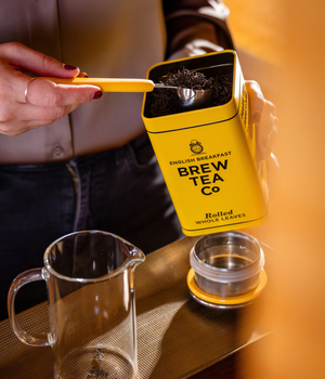 A tin of Brew tea Company rolled whole leaves english breakfast tea is being scooped into a tea pot for one, ready to brew a cup of tea.